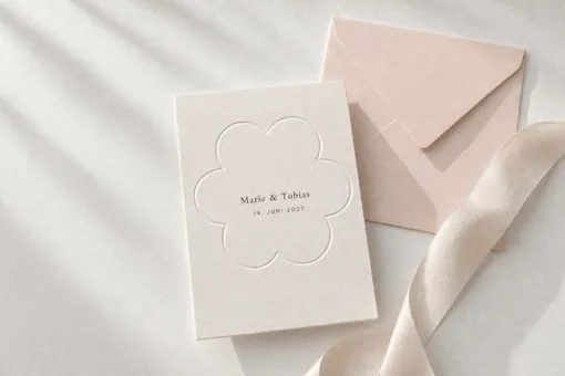 Visualisation: a cream card with a flower-shaped embossed window, the couple's names printed inside it, beside a blush envelope.